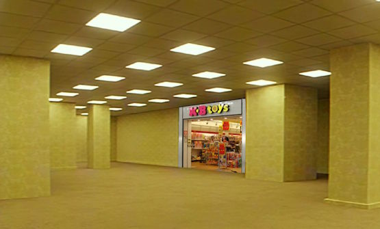 A typical yellow ''backrooms'' hallway, but one of the doorway openings has a fully stocked KB Toys inside it.