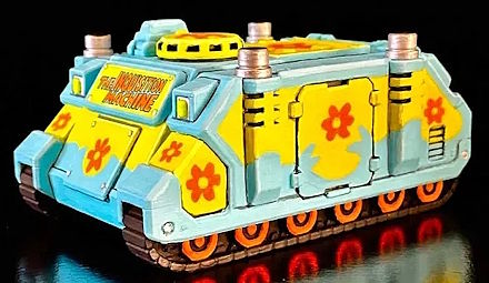 A custom-painted Warhammer 40,000 Adeptus Astartes Rhino transport vehicle miniature custom-painted as the Scooby-Doo Mystery Machine. The chassis has a light blue and yellow color scheme decorated with orange flowers.

A front placard plaque: THE INQUISITION MACHINE